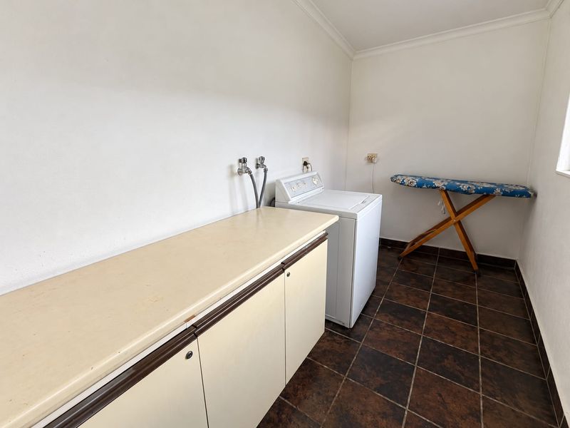 Functional laundry room featuring built-in cabinetry with laminate countertop, plumbing connections for appliances, and durable tiled flooring.