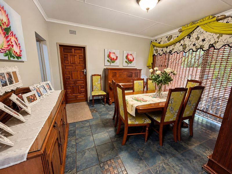 A dining room featuring tiled flooring, a wooden door, and large windows with blinds, providing a functional space for family meals.