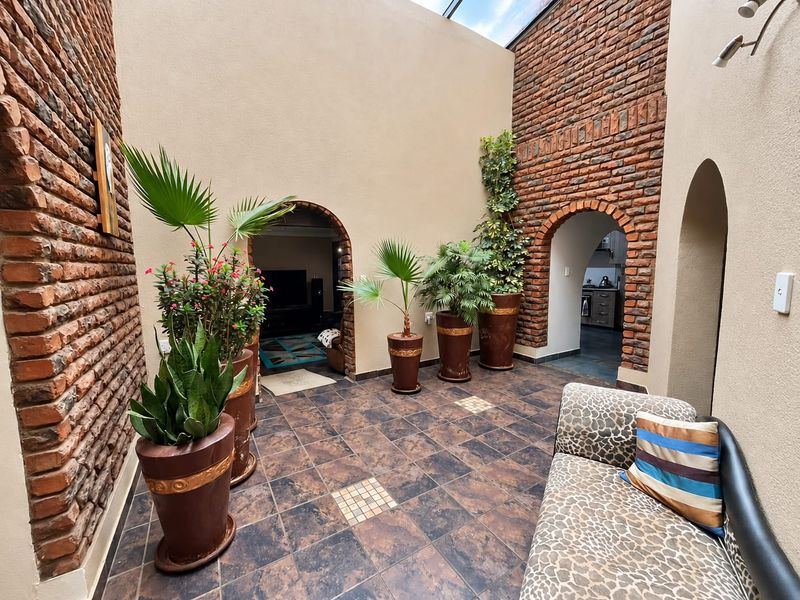 An enclosed courtyard or atrium featuring exposed brick walls, tiled flooring, and a skylight, providing access to adjacent living and kitchen areas.