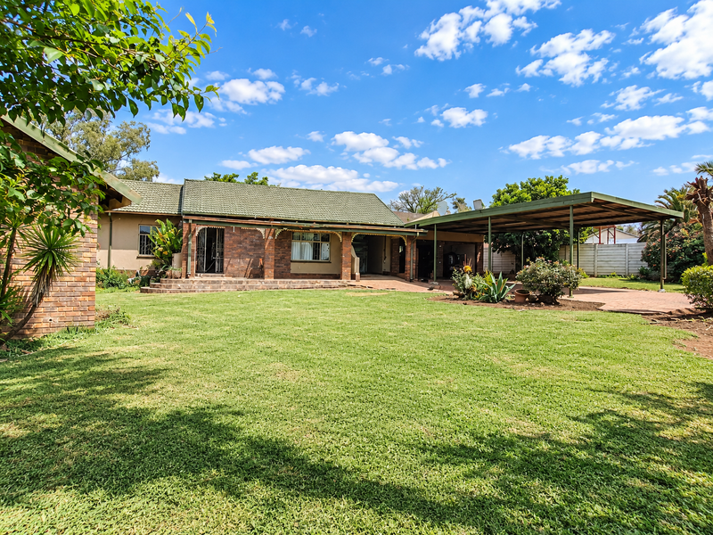 Spacious rear garden featuring a large lawn, covered patio area, and a functional carport with paved driveway access.