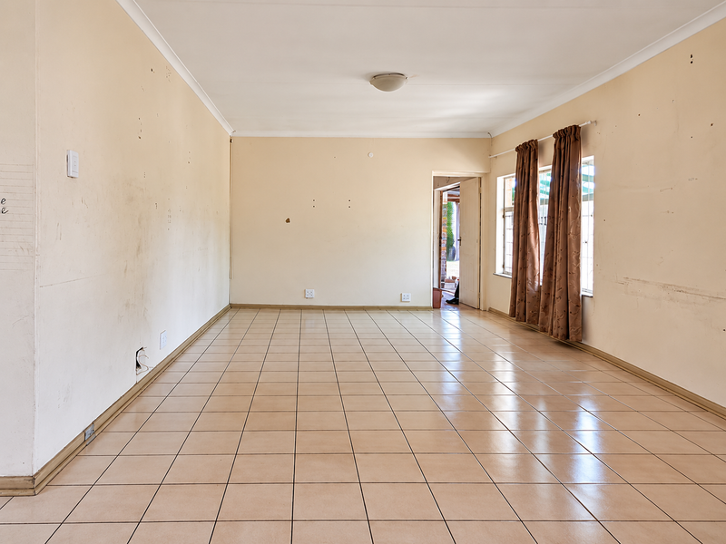 A spacious, empty living area featuring neutral ceramic floor tiles, coved ceilings, and natural light, ready for a fresh coat of paint and new finishes.