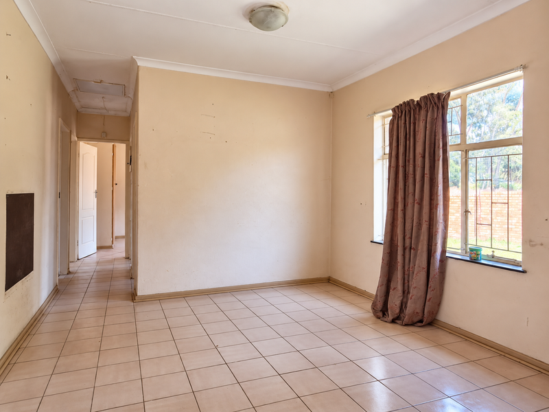 An empty living room featuring tiled flooring, neutral walls, and a window with security bars, offering a blank canvas for renovation.