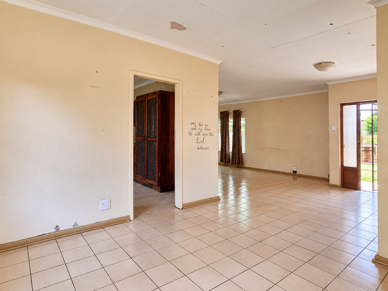 Spacious open-plan living area featuring neutral ceramic floor tiles, ample natural light, and direct access to the exterior through a wooden door.