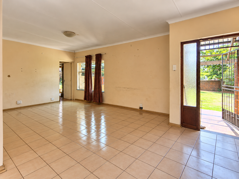Spacious, empty living area featuring tiled flooring and direct access to the garden through a secure glass panel door.