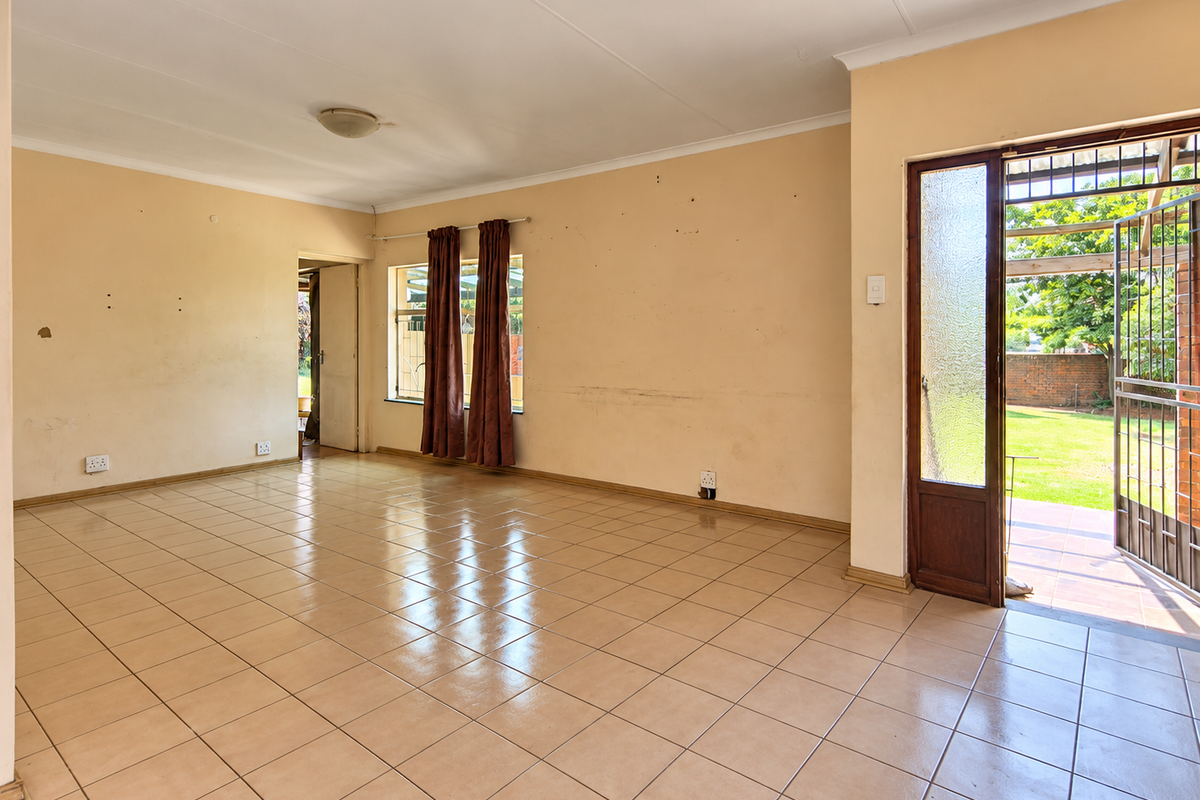 Spacious, empty living area featuring tiled flooring and direct access to the garden through a secure glass panel door.