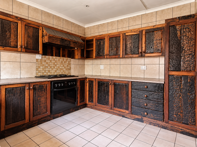 A dated kitchen featuring rustic dark wood cabinetry, built-in oven, hob, and tiled finishes, offering significant potential for a modern renovation.