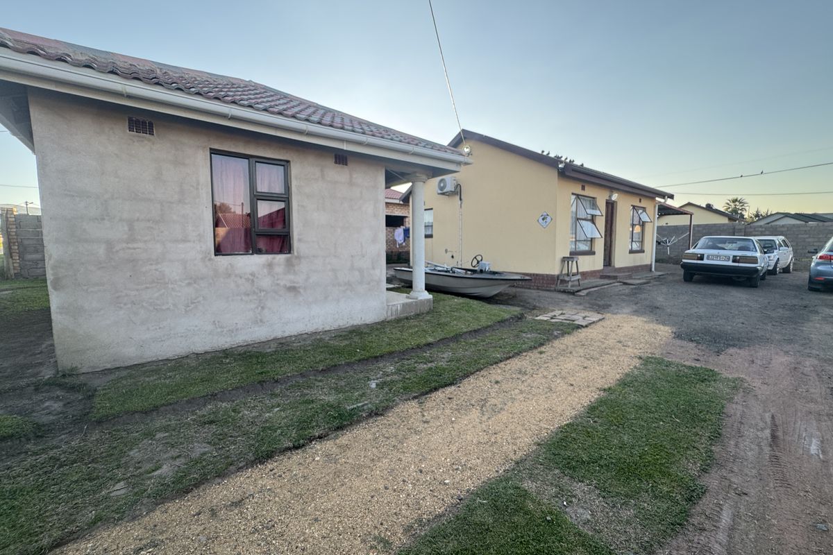 Rear view of the property showing two residential structures with tiled roofs, aluminium window frames, and an installed air conditioning unit.