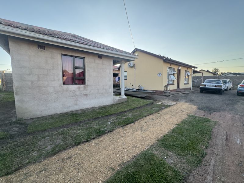 Rear view of the property showing two residential structures with tiled roofs, aluminium window frames, and an installed air conditioning unit.