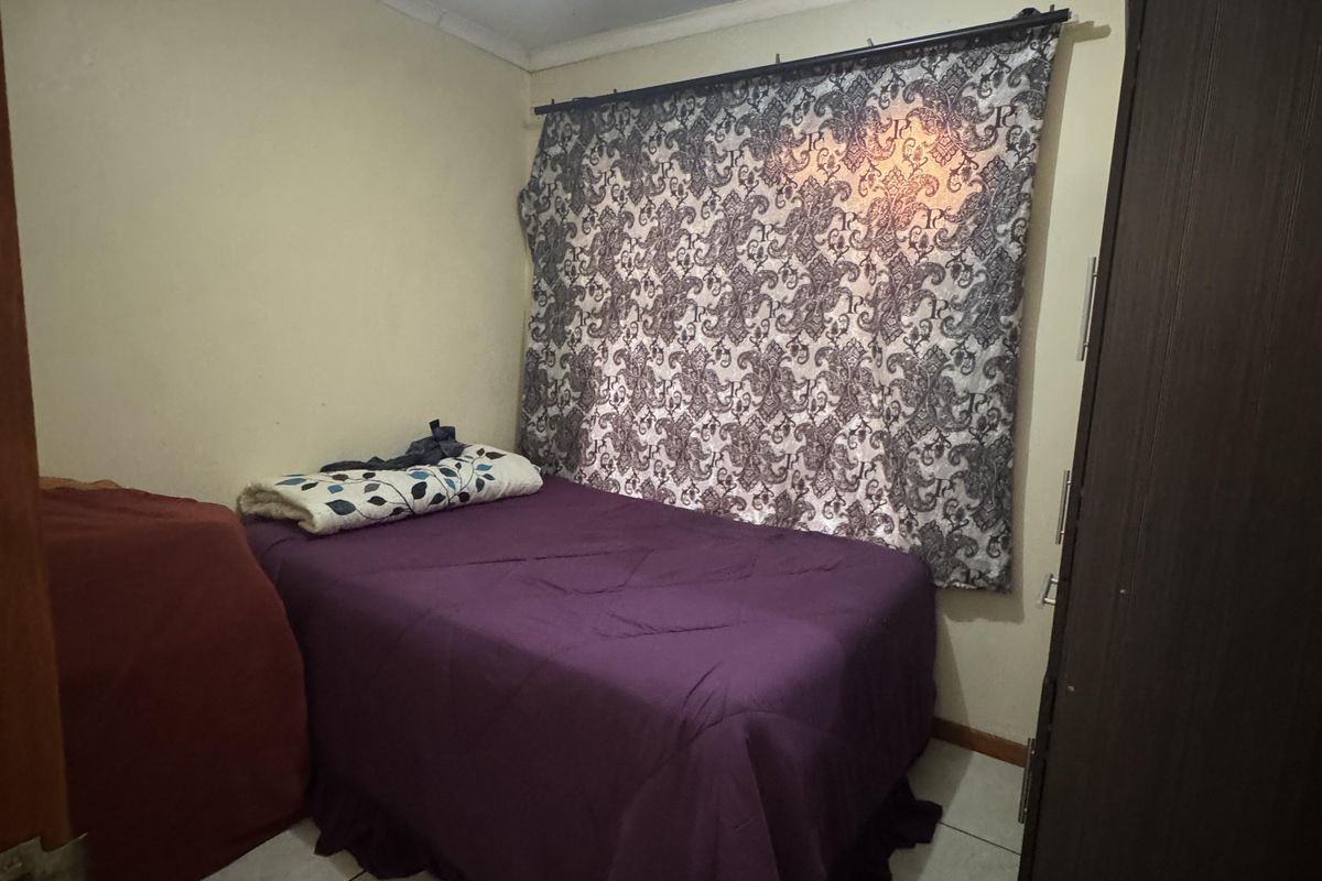 A compact bedroom featuring tiled flooring and a window with a curtain rod. The room requires cosmetic updates to improve its overall condition.