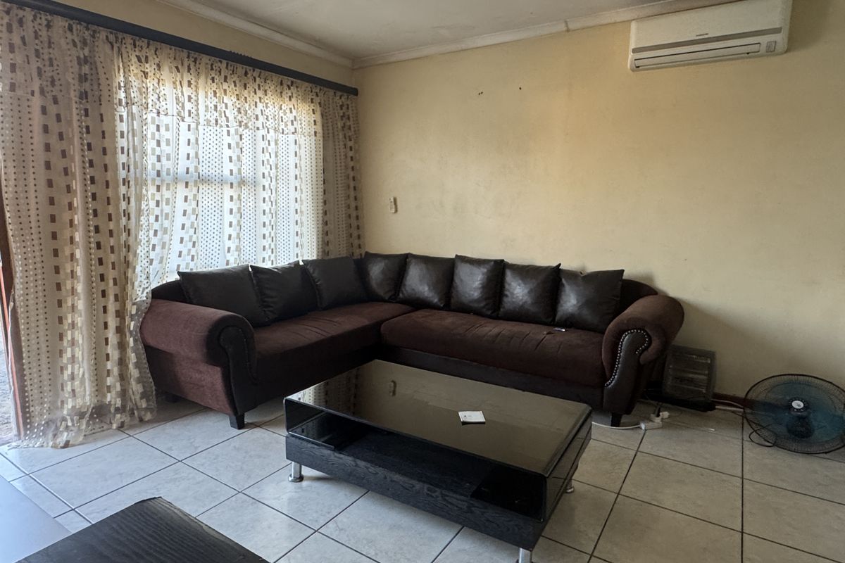 A living room featuring tiled flooring and a wall-mounted air conditioning unit, requiring cosmetic updates to the wall finishes.
