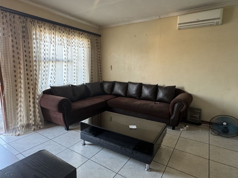 A living room featuring tiled flooring and a wall-mounted air conditioning unit, requiring cosmetic updates to the wall finishes.