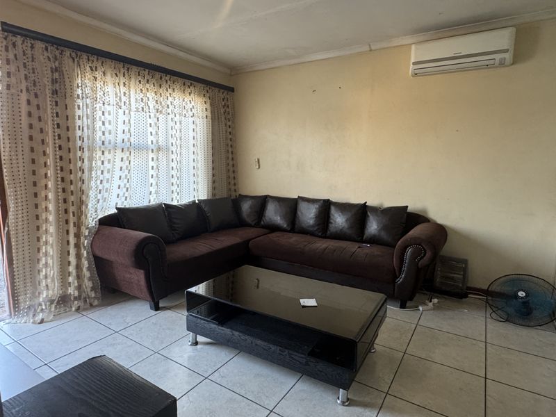 A living room featuring tiled flooring and a wall-mounted air conditioning unit, requiring cosmetic updates to the walls and ceiling.