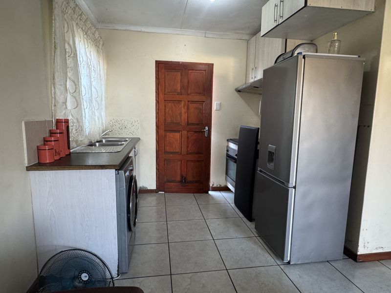 A functional kitchen featuring tiled flooring, built-in cabinetry, and a stainless steel sink, requiring cosmetic updates to improve its overall condition and appeal.