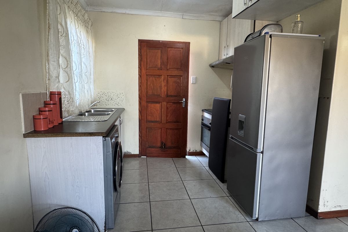 A functional kitchen featuring tiled flooring, built-in cabinetry, and a stainless steel sink, requiring cosmetic updates to improve its overall condition and appeal.