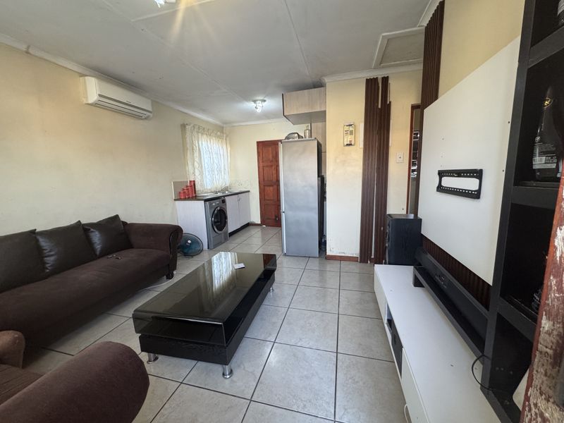 Open-plan living area featuring tiled flooring, a compact kitchen kitchenette, and a wall-mounted air conditioning unit.