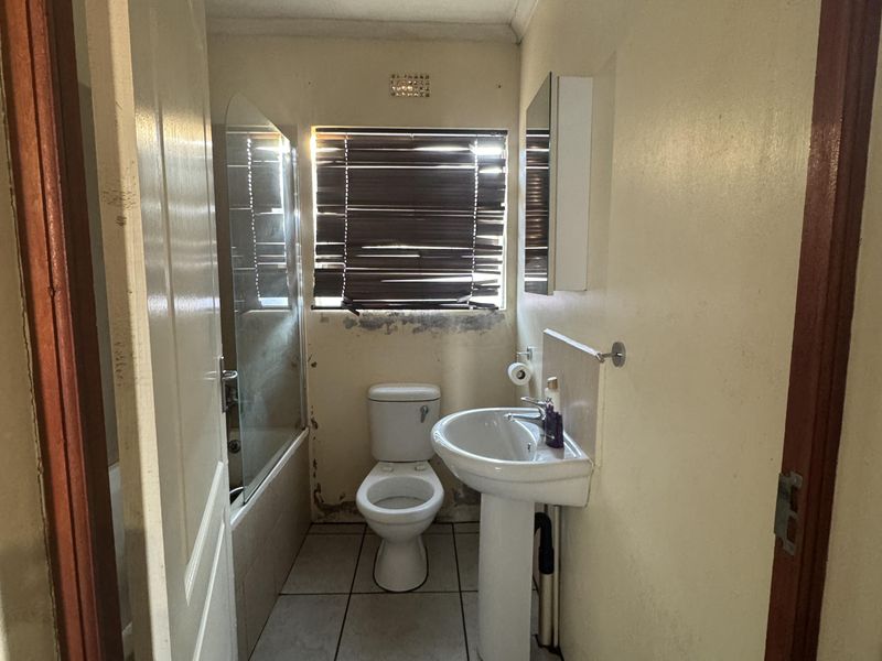 A compact bathroom featuring a pedestal basin, toilet, and bathtub with a glass screen, currently requiring cosmetic updates and wall repairs.