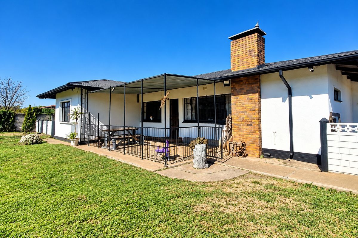 Rear view of the house featuring a covered patio area, brick chimney, and a spacious lawn.