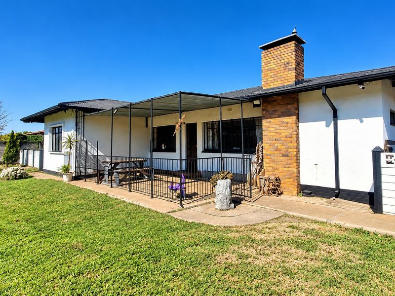 Rear view of the house featuring a covered patio area, brick chimney, and a spacious lawn.