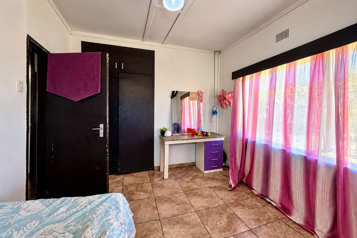 A bedroom featuring tiled flooring and built-in cupboards, offering a functional space with natural light.