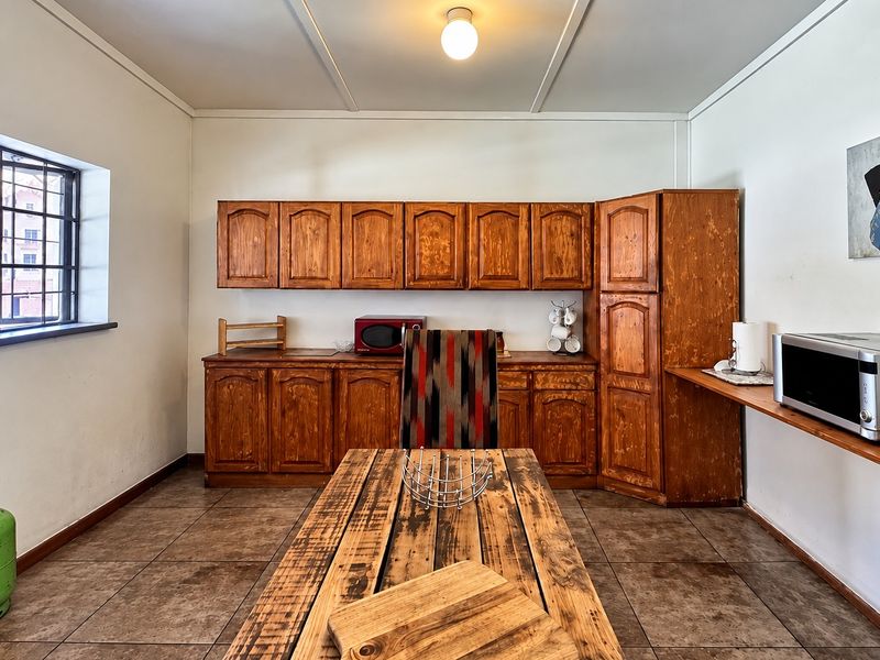 A kitchen area featuring dated wooden cabinetry, tiled flooring, and security bars on the window, offering potential for a modern renovation.