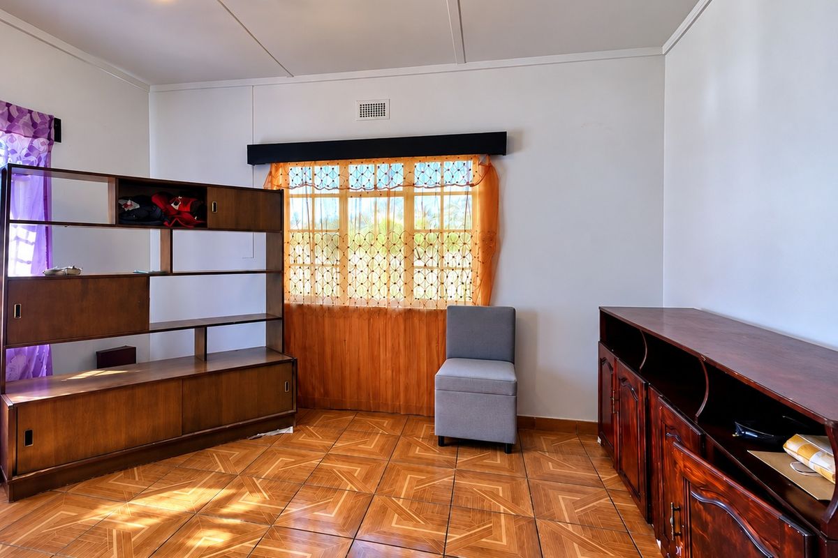 A living room featuring patterned tiled flooring, a ceiling light fixture, and a window with a wooden pelmet.