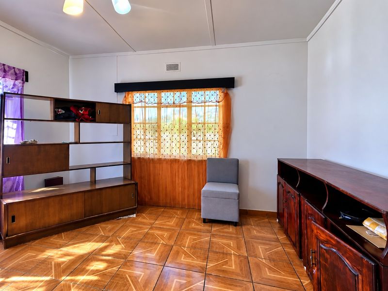 A living room featuring patterned tiled flooring, a ceiling light fixture, and a window with a wooden pelmet.