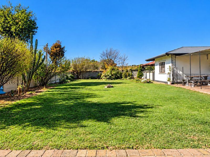 A spacious backyard featuring a well-maintained lawn, perimeter boundary wall, and a covered patio area attached to the main house structure.
