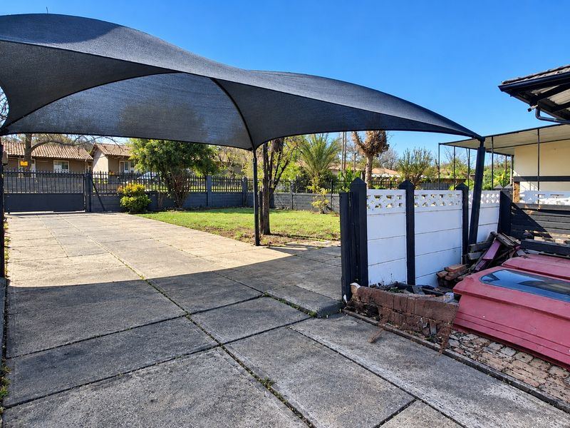 Front exterior area featuring a paved driveway, shade sail structure, and perimeter walling with gated access.