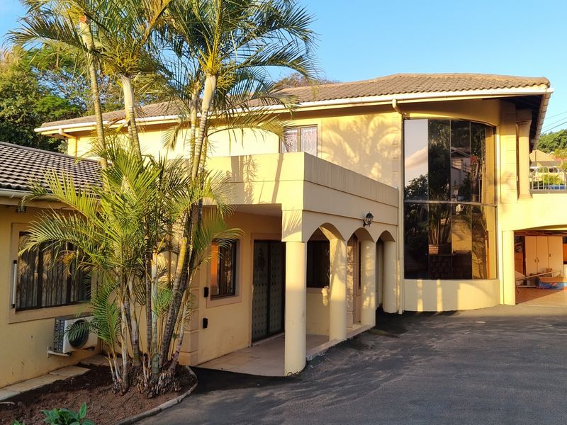 Front elevation of a multi-story house featuring an arched covered entrance, large floor-to-ceiling windows, and an asphalt driveway.