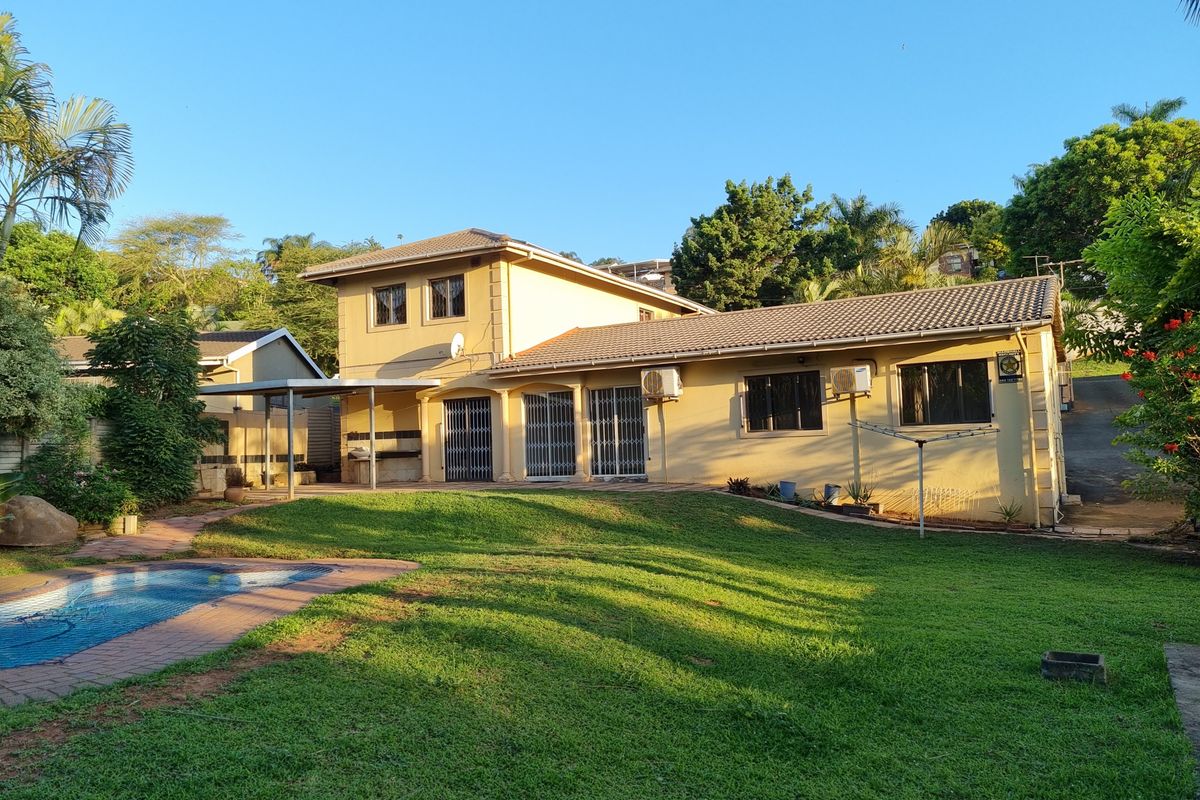 Rear view of the house featuring a swimming pool, paved patio area, and a well-maintained garden with established trees.