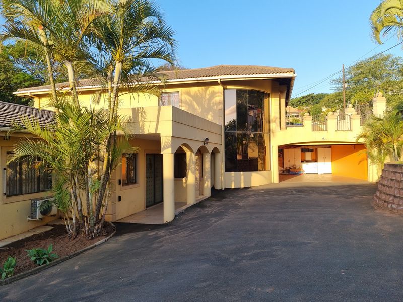 Front elevation of a multi-level residence featuring an arched entrance, double-height glass windows, and a paved driveway leading to a covered parking area.