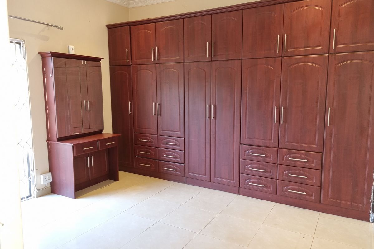 Spacious bedroom featuring extensive wall-to-wall built-in wooden cabinetry with an integrated vanity unit and neutral tiled flooring.