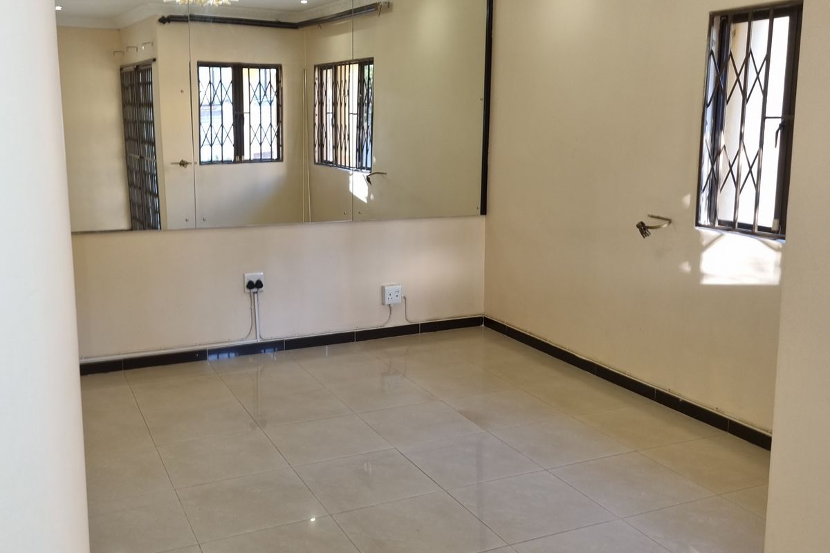 A bright, empty living area featuring large format floor tiles, recessed lighting, decorative ceiling roses, and a large wall-mounted mirror.