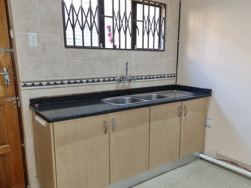 A functional scullery area featuring a double stainless steel sink, granite countertops, and ample under-counter cabinetry with tiled finishes.