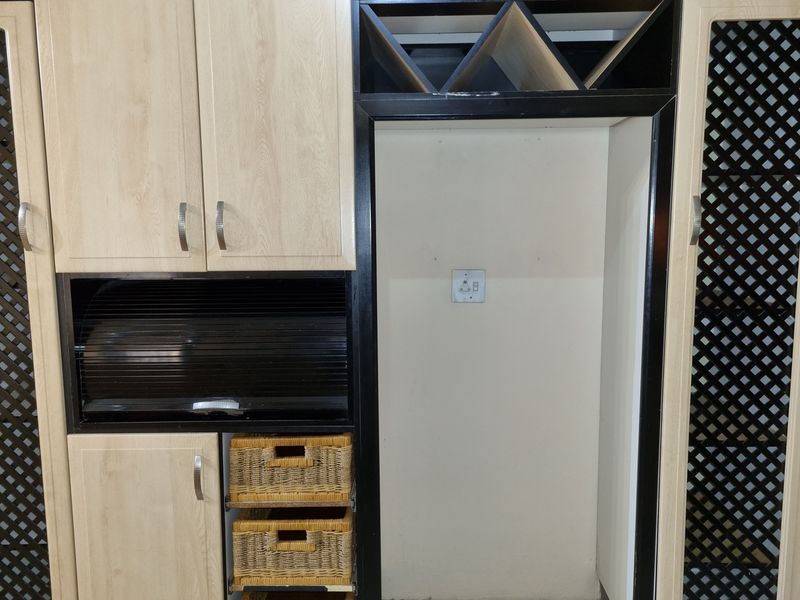 A kitchen storage unit featuring light wood-grain cabinetry, a dedicated appliance recess, integrated wine rack, and pull-out storage baskets.