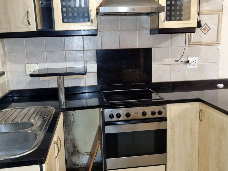 A functional kitchen featuring granite countertops, built-in oven and hob, and stainless steel extractor fan, currently requiring repairs to the lower cabinetry.