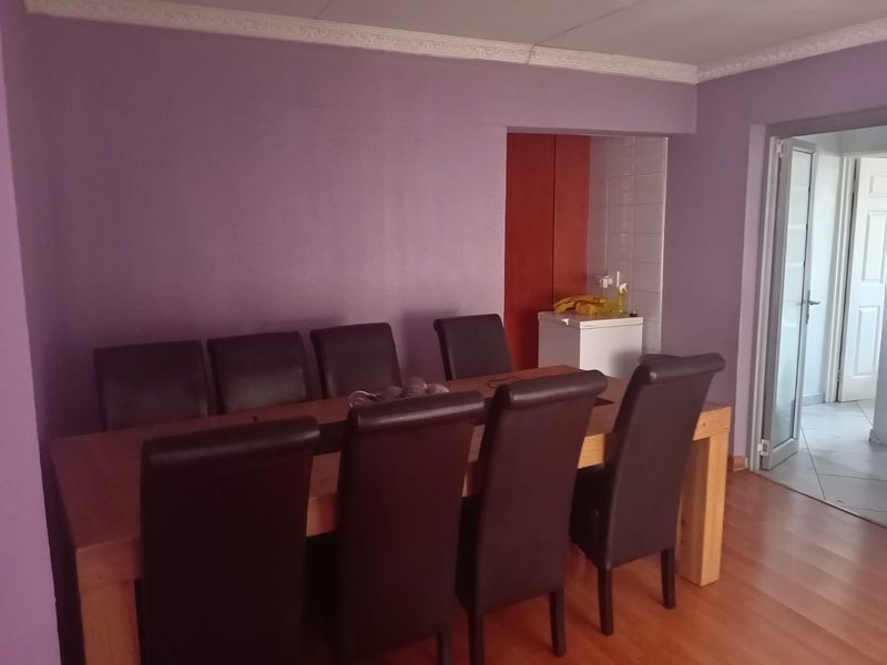 Dining room featuring laminate flooring and decorative crown molding, with an adjacent alcove area containing a tiled splashback.