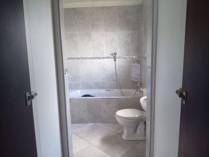 A functional bathroom featuring a built-in bathtub with shower mixer and a standard toilet, finished with neutral wall and floor tiling.