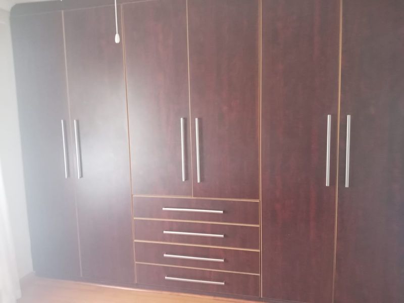 A bedroom featuring dark wood built-in cupboards with integrated drawers and modern metal handles.