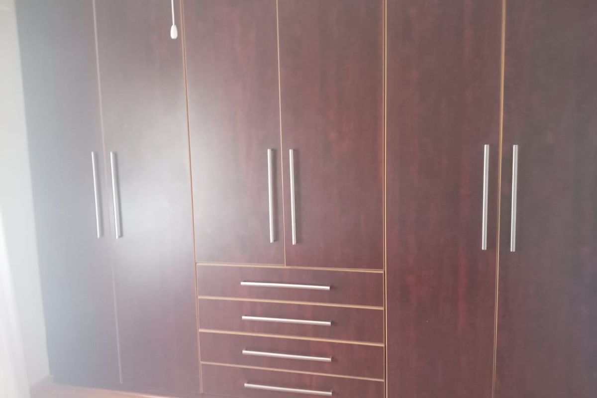 A bedroom featuring dark wood built-in cupboards with integrated drawers and modern metal handles.