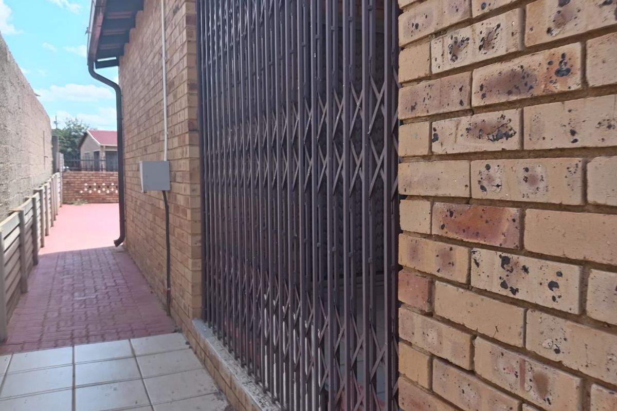 A side exterior view of the property featuring face brick walls, a security gate, and a paved walkway leading to the rear area.