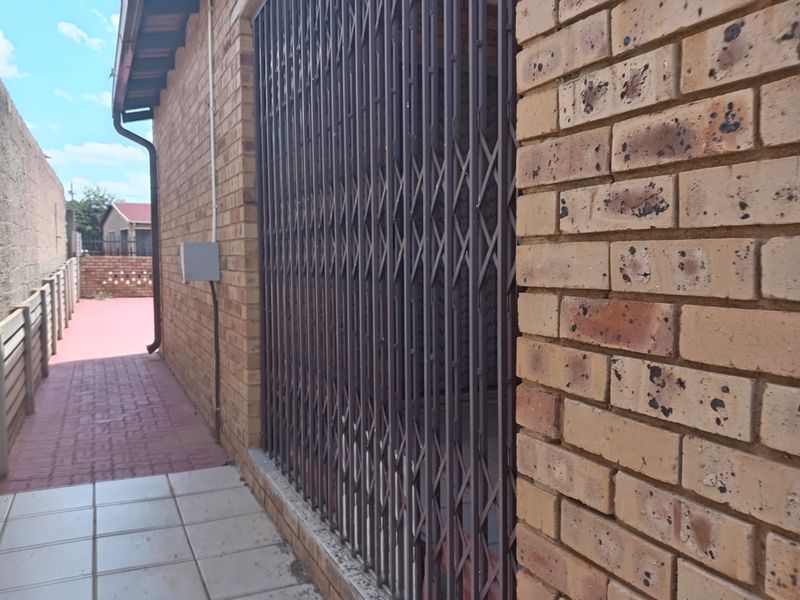A side exterior view of the property featuring face brick walls, a security gate, and a paved walkway leading to the rear area.