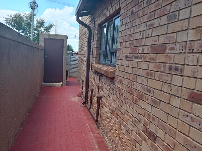 A side exterior view of the property featuring face brick walls, a paved walkway, and a secure boundary wall.