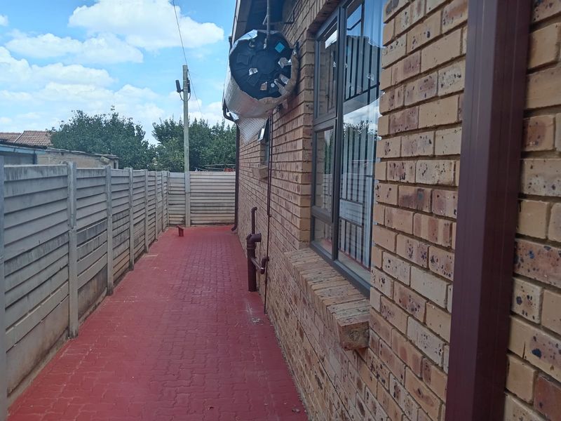 Side exterior view of the property featuring a red paved walkway, brick walling, and an externally mounted geyser unit.