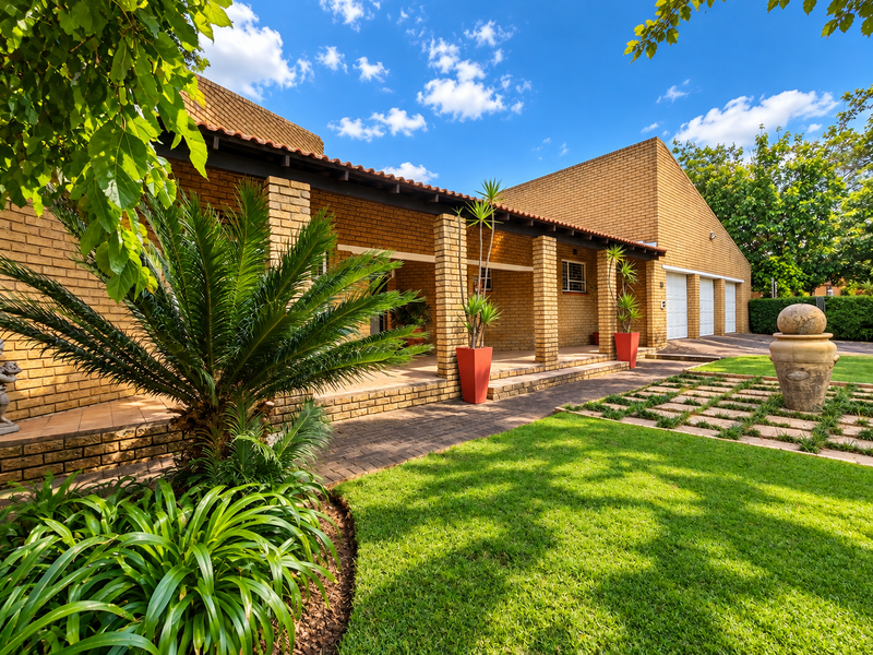 A well-maintained brick house featuring a covered patio, triple garage, and a beautifully landscaped front garden with a paved walkway.