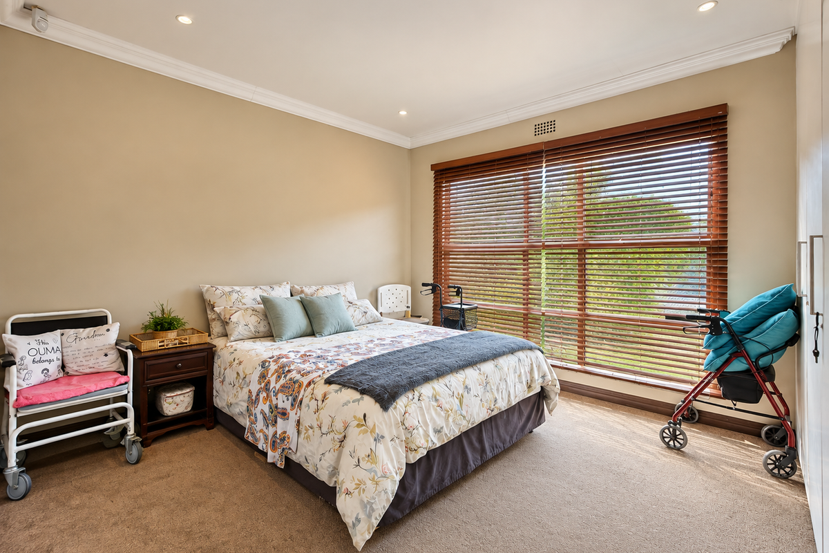 A well-maintained bedroom featuring neutral walls, carpet flooring, built-in cupboards, and large windows with timber venetian blinds providing natural light.