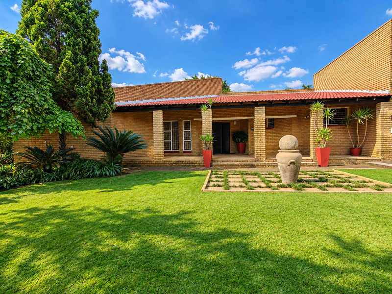 A well-maintained rear exterior view featuring a brick facade, a covered patio area with brick pillars, and a neatly landscaped garden.