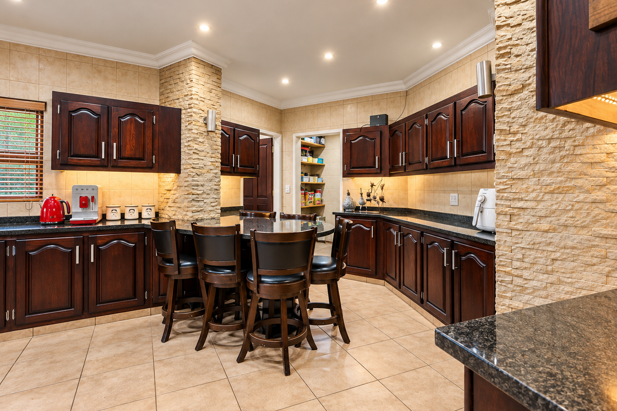 Spacious kitchen featuring dark wood cabinetry, granite countertops, and a unique stacked stone feature wall, with an adjoining scullery area.