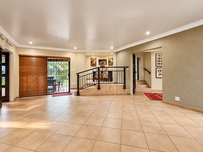 Spacious open-plan living area featuring ceramic tile flooring, recessed lighting, and a raised dining platform with a decorative metal railing.