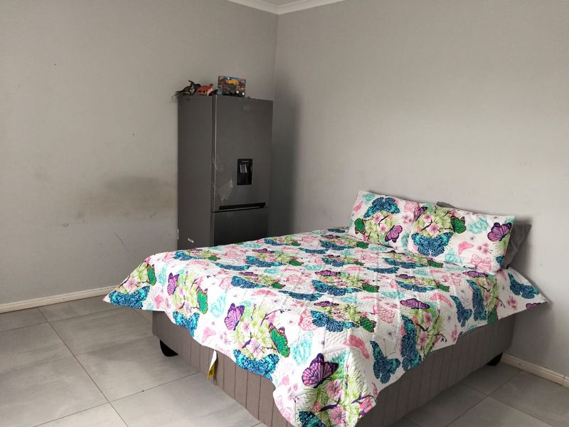 A bedroom featuring tiled flooring and neutral wall finishes, showing some signs of wear on the wall surface.